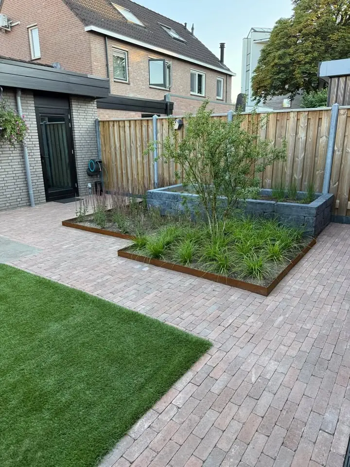 Achtertuin met een terras van gebakken klinkers, kunstgras, borders met een rand van cortenstaal en een verhoogde border langs de schutting