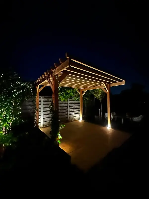 Houten pergola bij avond met klimplanten en grondspots bij de palen