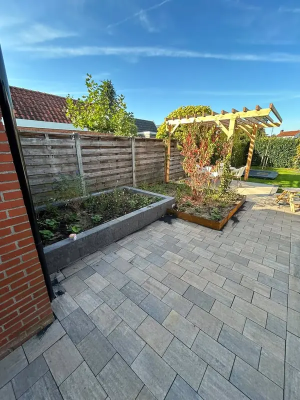Terras van grijze tegels met een verhoogde border, een plantenbak van cortenstaal en een houten pergola
